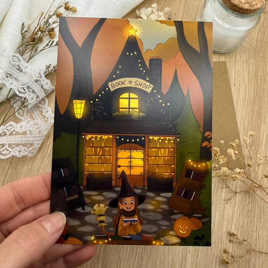 Postkarte „Bookshop Witch“ Herbstliche Hexe vor Buchladen | Magische Herbstkarte mit Kürbis & Lichterglanz